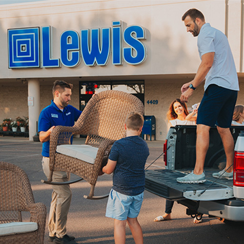 A lewis employee helps a father and son load a lawn chair into a vehicle.