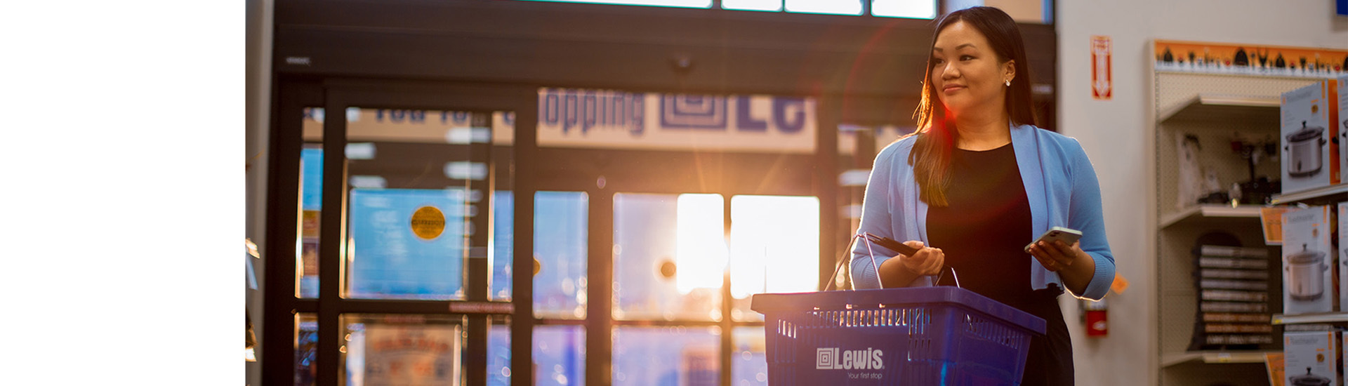 A woman walks into lewis with a basket and her phone in hand.
