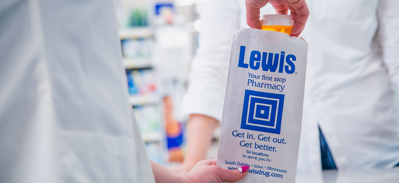 A pharmacist puts a bottle into a prescription bag.